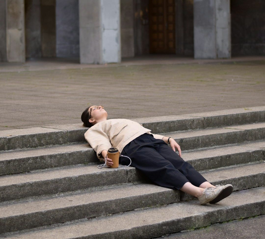 man in brown hoodie and black pants sitting on gray concrete stairs