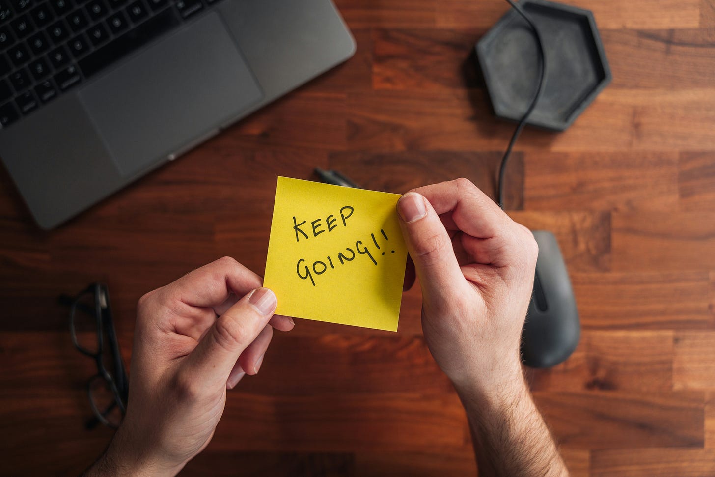 A person holding a yellow sticky note that says "keep going." 