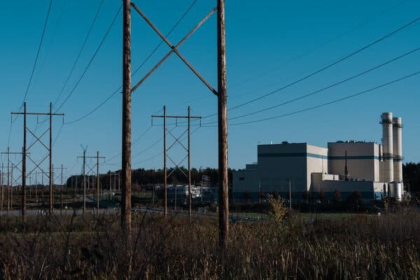 Power lines run in front of a power plant with smoke stacks visible on the right.