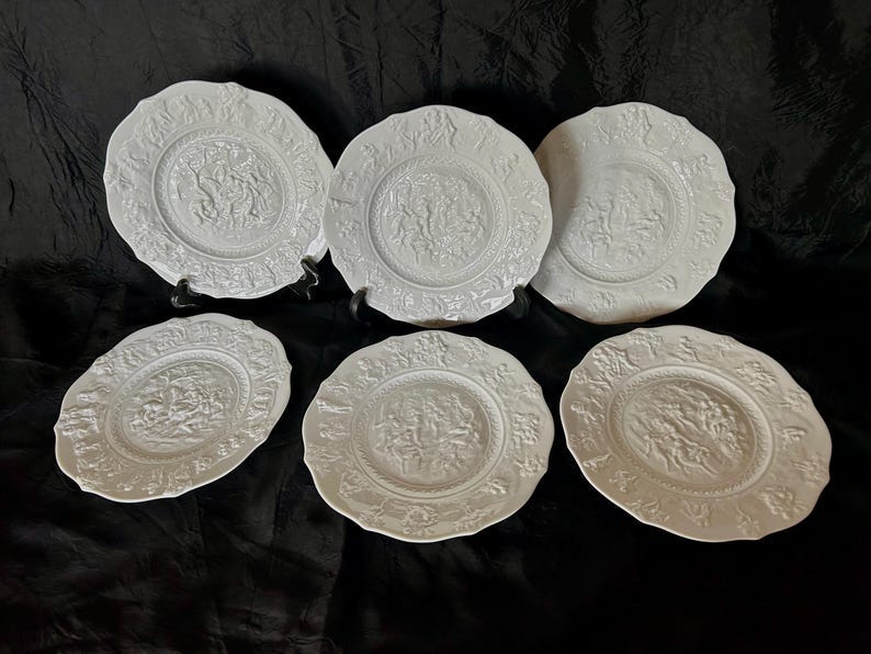 May include: Six white ceramic plates with raised embossed designs. The plates have a scalloped edge and are arranged in two rows of three.