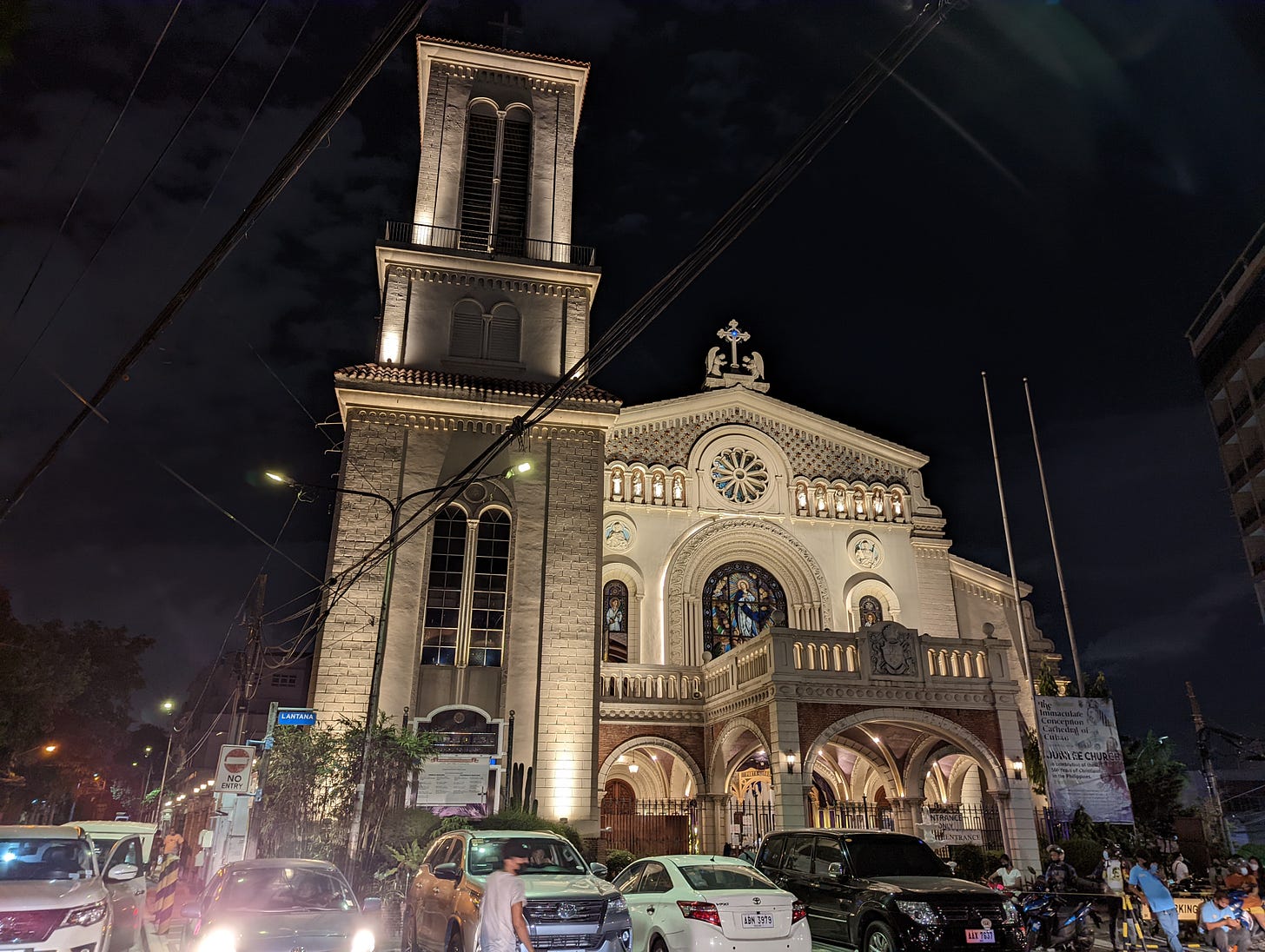 The well-lit facade of the Cathedral of Cubao with parked cars in front of it