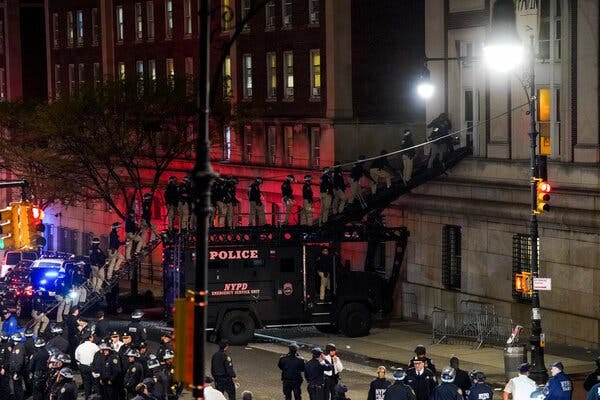 Police officers are lined up on a ladder that leads up to and across a police van and then to a second-story window of a building. More officers are gathered in a street in front of the building. Police officers are lined up on a ladder that leads up to and across a police van and then to a second-story window of a building. More officers are gathered in a street in front of the building.