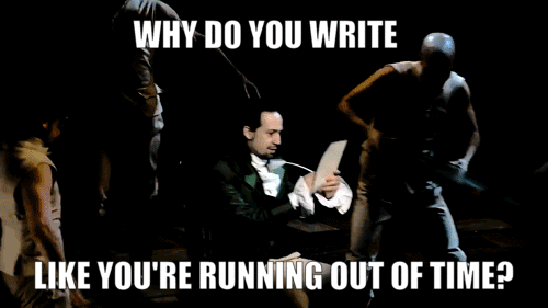 the original cast from Hamilton singing and dancing around a man seated, wearing a coat and writing at a desk
