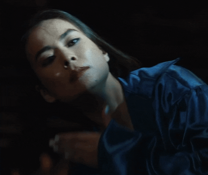 Gif do clipe Working For The Knife, da Mitski. Ela está passando a mão na frente do rosto e a cada vez que a mão passa sua expressão se altera, ora um sorriso maníaco e ora um semblante sério
