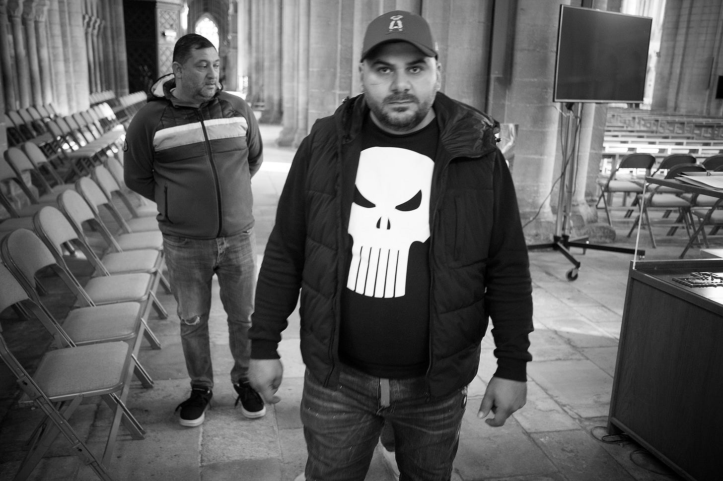 two men standing in Ely cathedral. One is wearing a punisher t-shirt. Black and white photo.