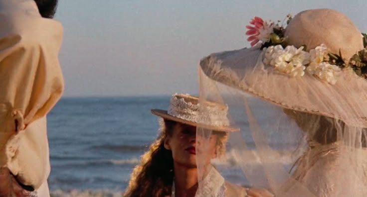 This may contain: two women standing on the beach wearing hats and veils