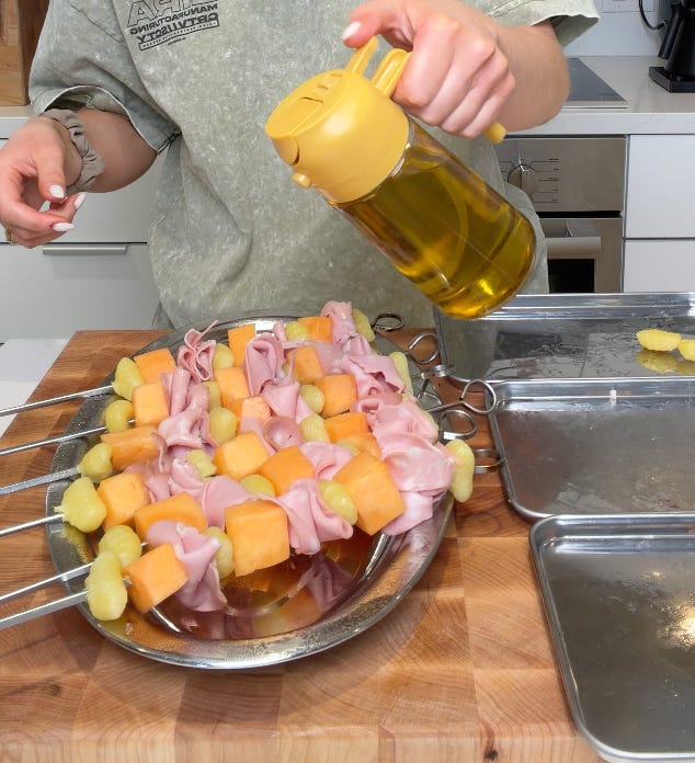 Assembled mortadella and gnocchi skewer held up to show the ruffled meat technique, Assembled mortadella, cantaloupe, and gnocchi skewers being brushed with avocado oil before grilling