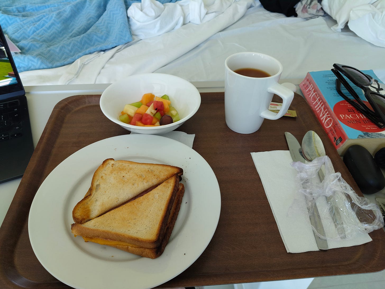 On a hospital tray sits a toasted ham and cheese sandwich, with a cereal bowl of fruit salad and a mug of black tea sitting beside it. My laptop with Love Island on the screen is just out of shot, and so is my unmade hospital bed. 