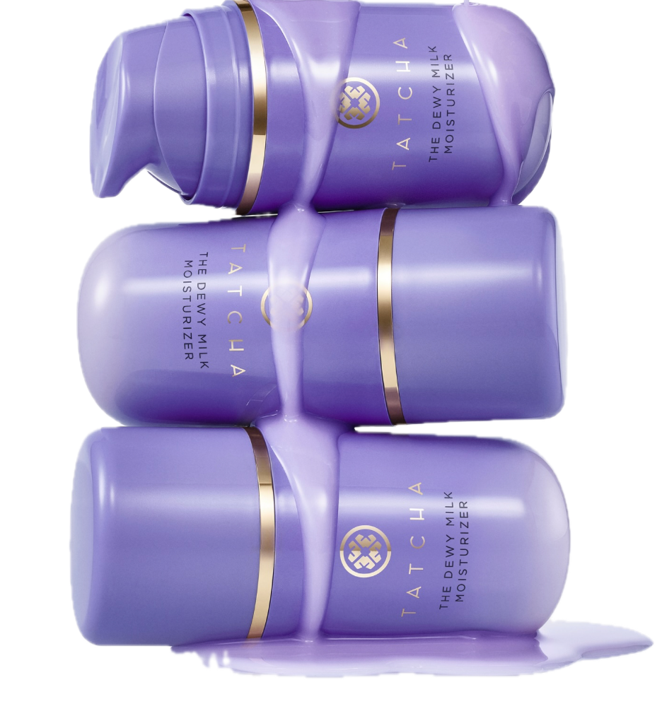 A texture-focused studio shot of three blue Tatcha The Dewy Milk Moisturizer bottles stacked horizontally. A thick, milky lavender liquid drips down the packaging to demonstrate the fluid, fast-absorbing consistency required for humid summer climates.