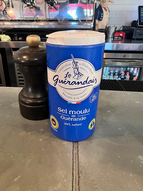 Three photos from Bouillon by Moulin: a seared salmon fillet over ratatouille, a tin of Le Guérandais sea salt on the bar, and a salmon tartare appetizer with toasted baguette on a red-rimmed bouillon plate.