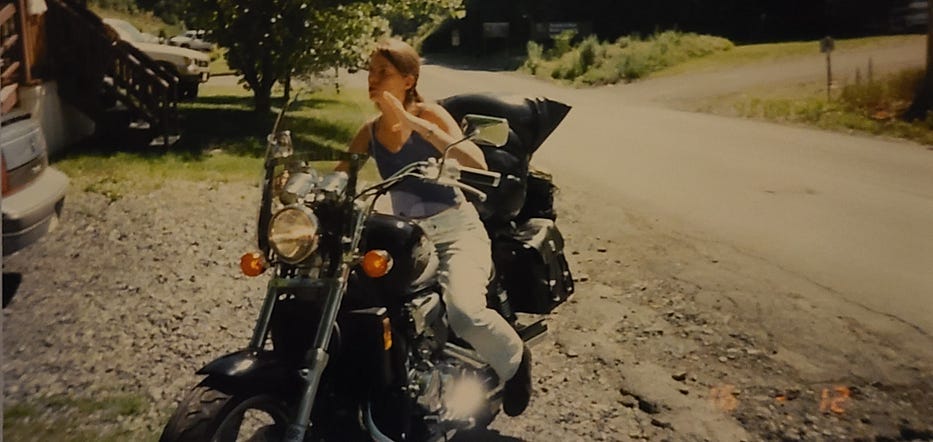 Photo of a thin young woman sitting on a large motorcycle.