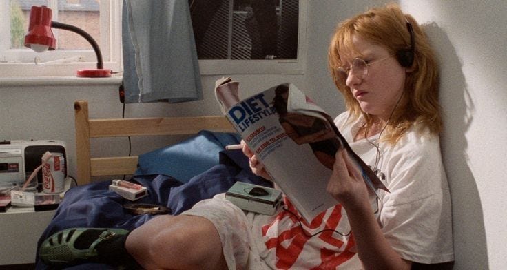 This may contain: a woman reading a magazine while sitting on a bed in a room with a window