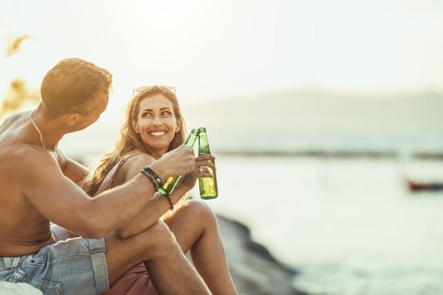 Pareja joven divirtiéndose y bebiendo cerveza en la playa junto al mar. Disfrutando de su amor.