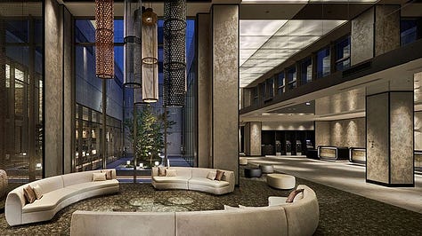 A modern and spacious hotel room with twin beds, a seating area with armchairs and a chaise lounge, a flat-screen TV, and large windows with sheer curtains. The accessible bathroom features grab bars, a handheld showerhead, and a shower chair.