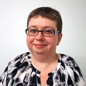 Author wearing back and white blouse smiles. She has short brown hair and is wearing funky glasses.
