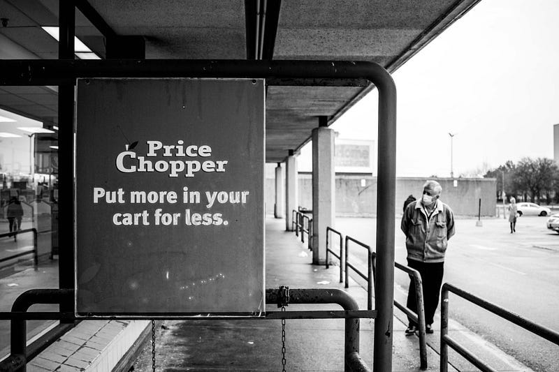 A elderly man in a mask walks peers into the empty price choppers. A Price Chopper sign reads: Put more in your cart for less
