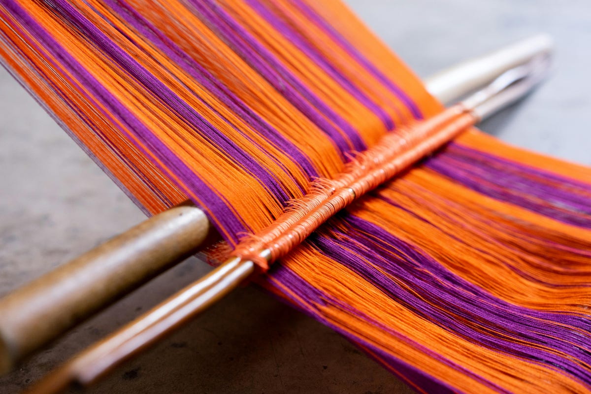 Primitive loom with orange and purple warp threads Primitive loom with orange and purple warp threads