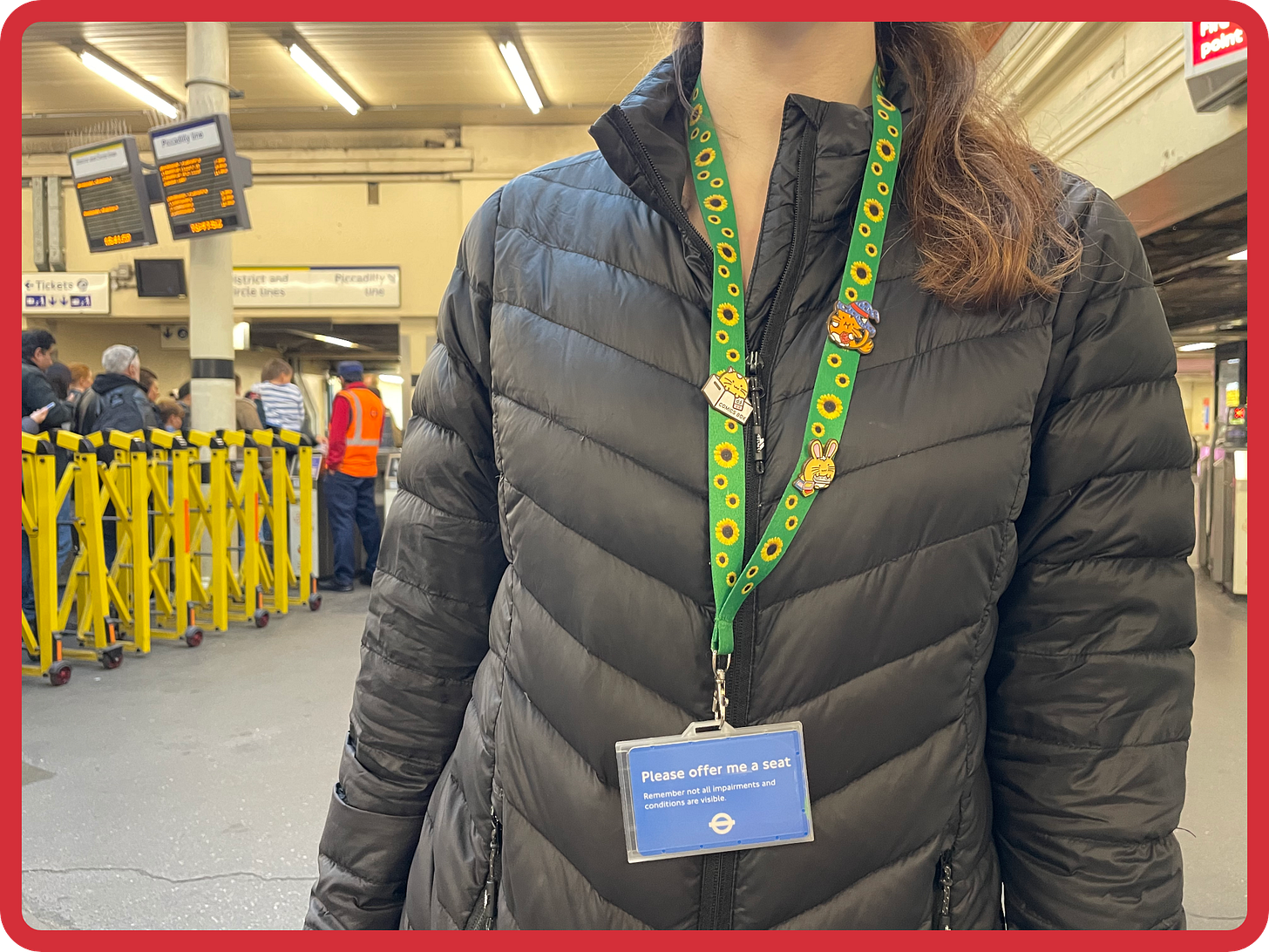A photo, below the neck, of a young woman wearing a green sunflower lanyard around her neck which holds a blue card which reads 'Please offer me a seat. Remember not all impairments and conditions are visible." She is wearing a black winter jacket. A photo, below the neck, of a young woman wearing a green sunflower lanyard around her neck which holds a blue card which reads 'Please offer me a seat. Remember not all impairments and conditions are visible." She is wearing a black winter jacket.