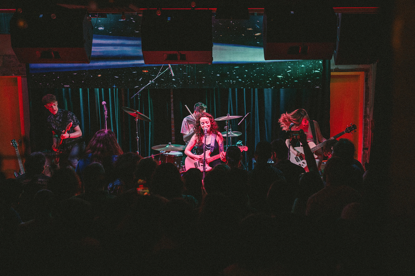 A photo of the four members of the band Flowerbomb performing to a packed room at the DC venue Comet Ping Pong. A photo of the four members of the band Flowerbomb performing to a packed room at the DC venue Comet Ping Pong.