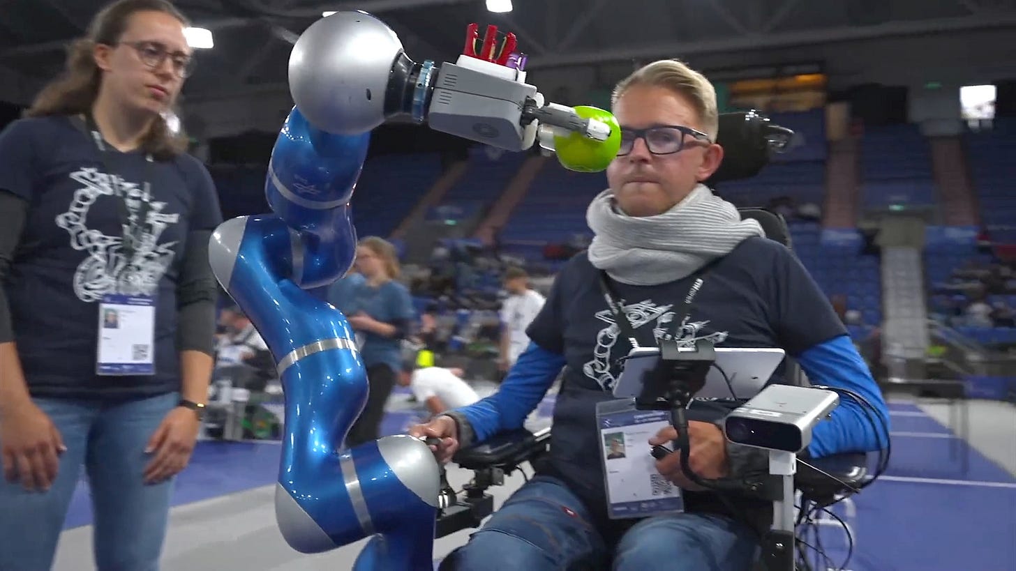 A man in a wheelchair with an attached robot arm holding an apple