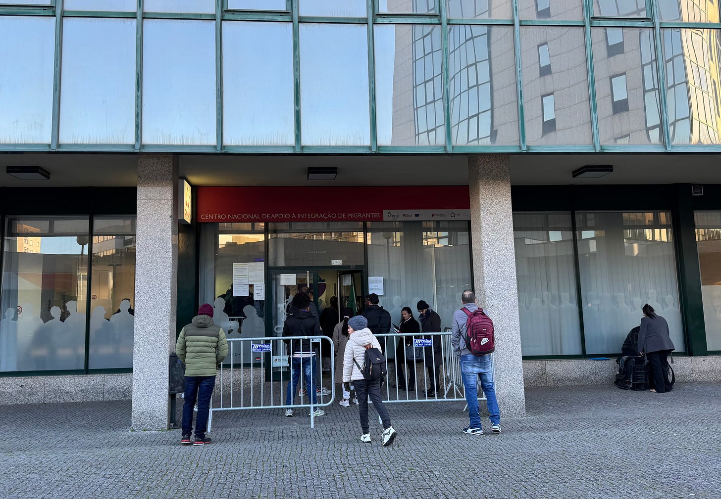 A small crowd stands outside a bureaucratic building. A small crowd stands outside a bureaucratic building.