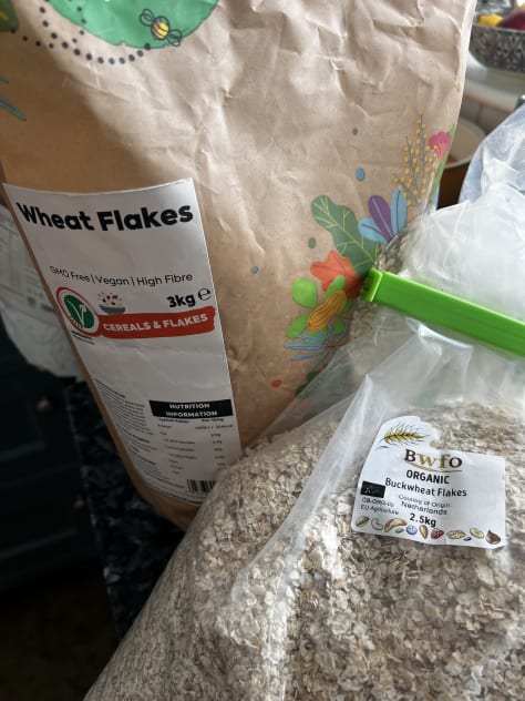 A selection of whole grain packages including rye, wheat, barley, buckwheat and flaxseed on a black stone worktop.