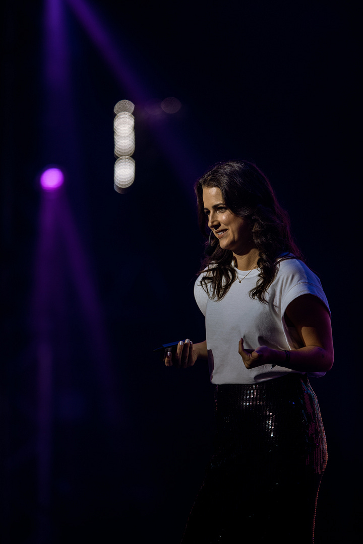 três fotos da Beatriz em cima do palco do RD Summit, usando uma camiseta branca e uma saia de brilhos. duas delas de perto, a outra de longe, com dimensão do palco grande e um slide com a definição de branding atrás dela