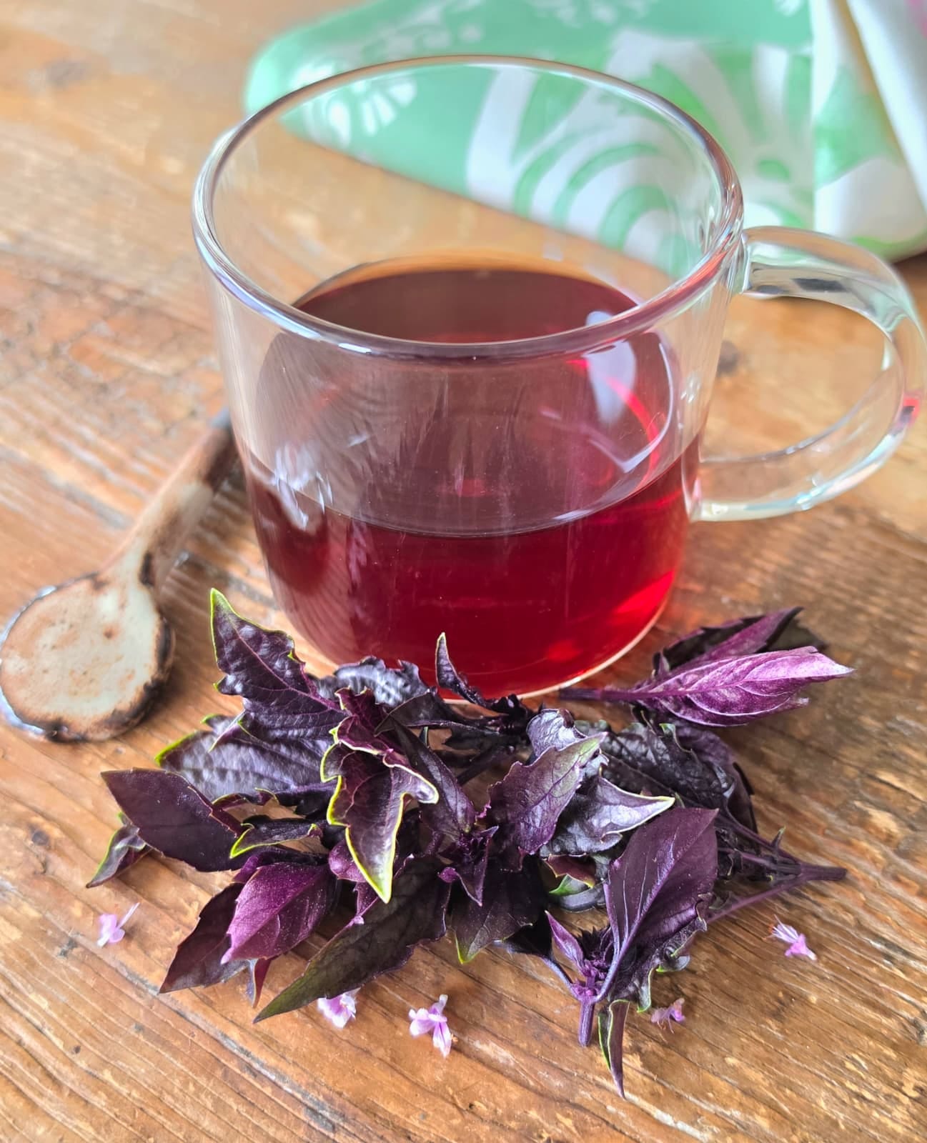 a cup of tea with basil leaves in front, a spoon alongside, and a kitchen towel in back a cup of tea with basil leaves in front, a spoon alongside, and a kitchen towel in back