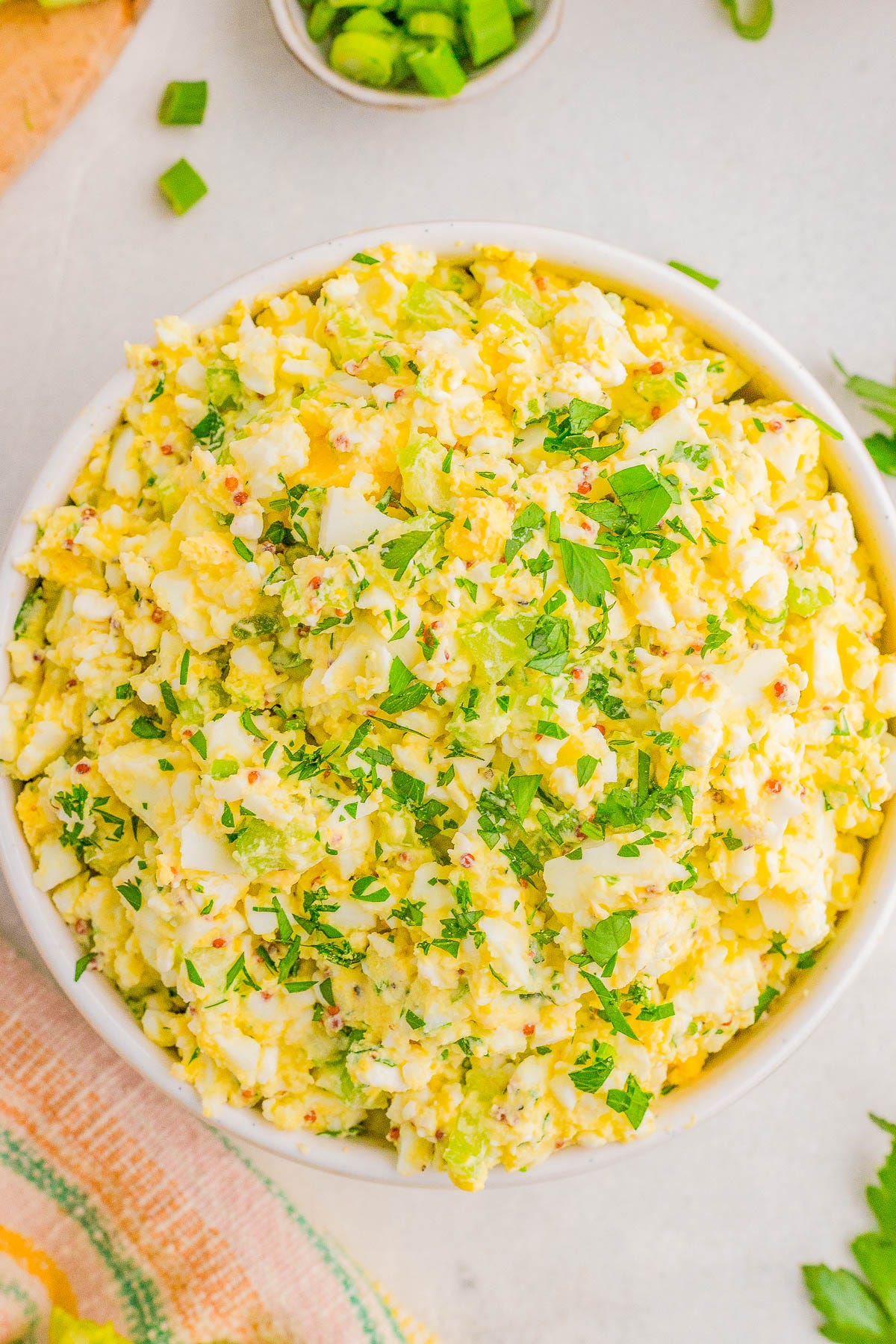 A bowl of egg salad garnished with chopped parsley, set on a light-colored surface. A bowl of egg salad garnished with chopped parsley, set on a light-colored surface.