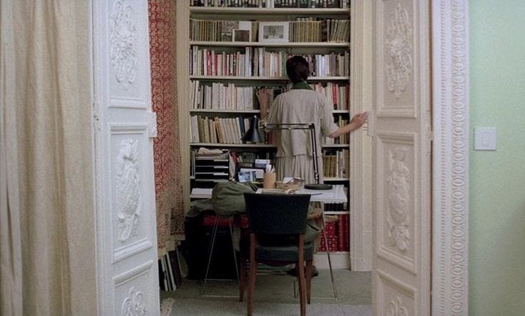This may contain: a woman standing in front of a bookshelf filled with lots of books next to a desk