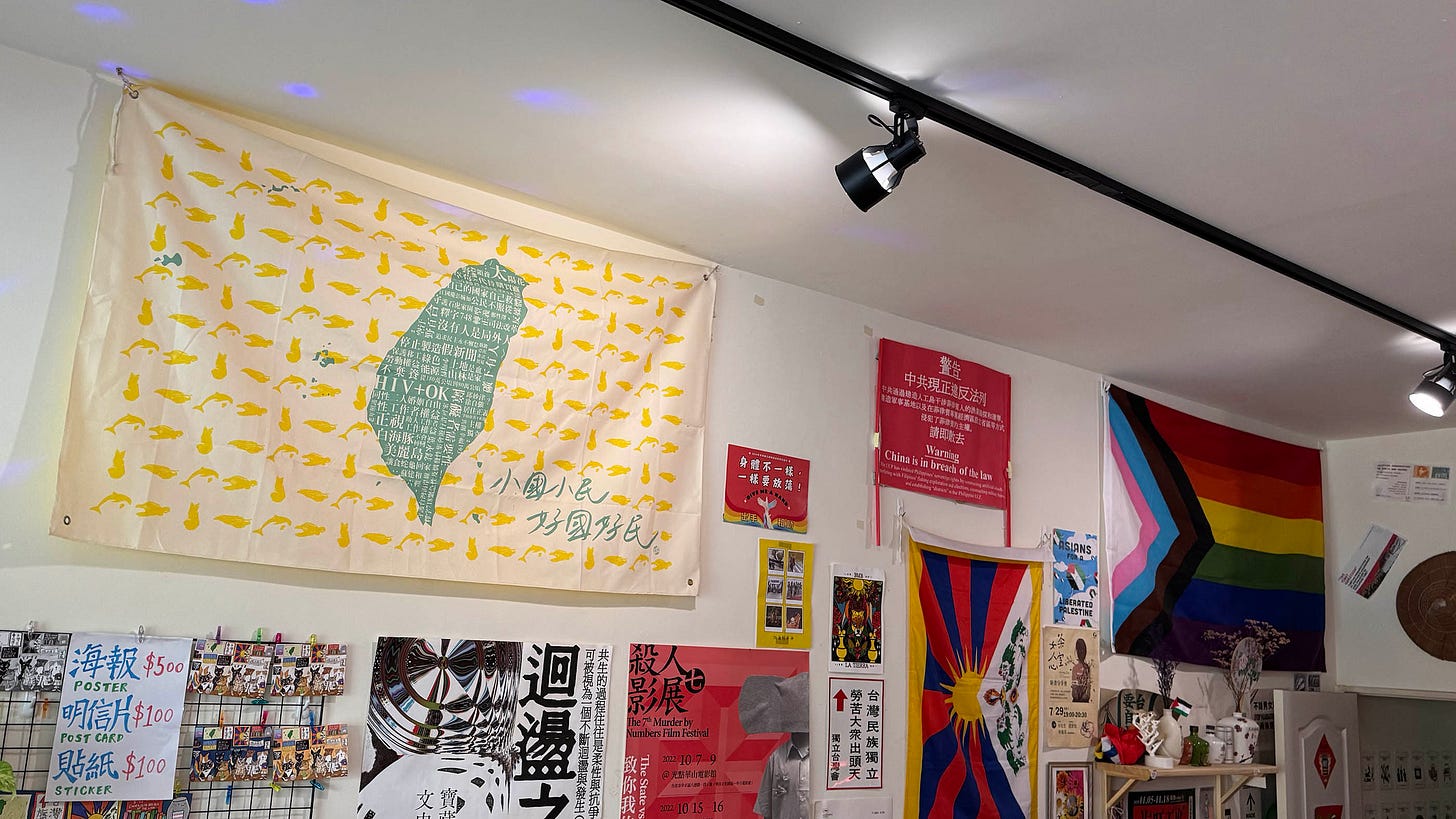 Horizontal photo of wall art at Daybreak in Wanhua. A large fabric sign shows the silhouette of Taiwan with animal symbols and Traditional Chinese characters 小國小民 好國好民. Other wall art include an L G B T Q I A flag and a free Tibet flag.