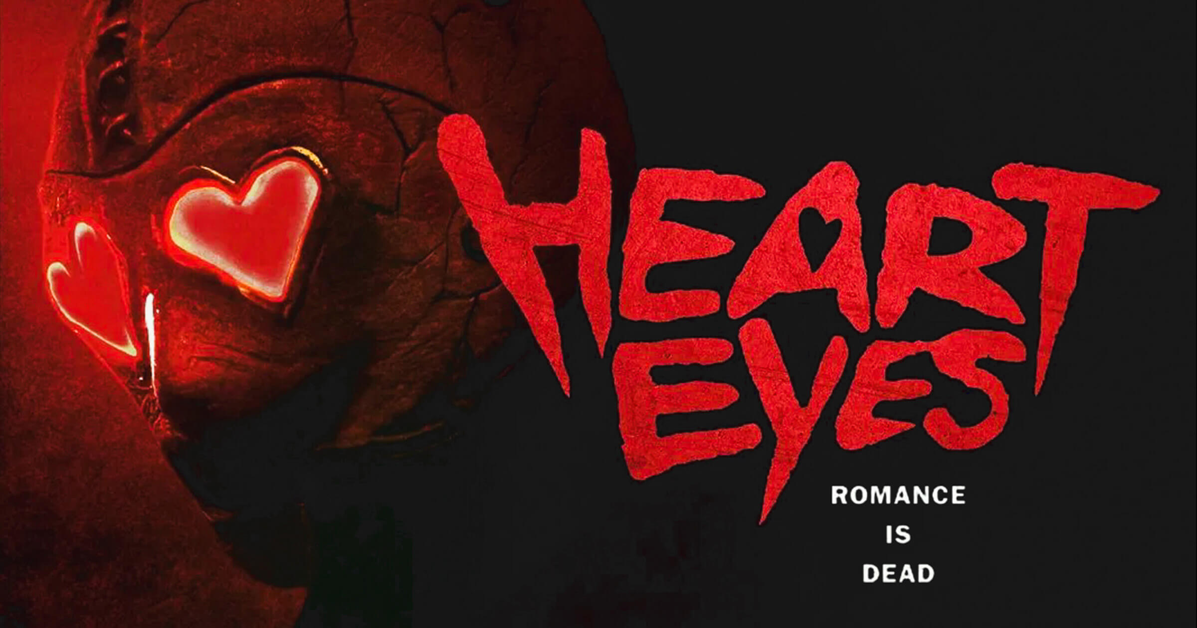 Poster art for Heart Eyes (2025) movie, A close-up of the killer's cracked mask with glowing red heart-shaped eyes peering back at us. The film’s title  is in bold red letters with the white tagline “Romance Is Dead.”