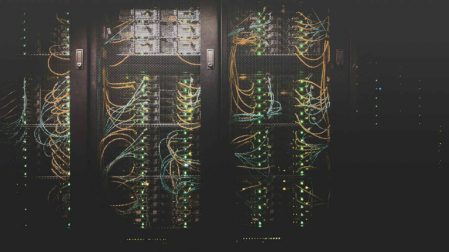 A picture of a row of three computer servers behind see-through doors. A tangle of cables and green LED lights can be seen. A picture of a row of three computer servers behind see-through doors. A tangle of cables and green LED lights can be seen.