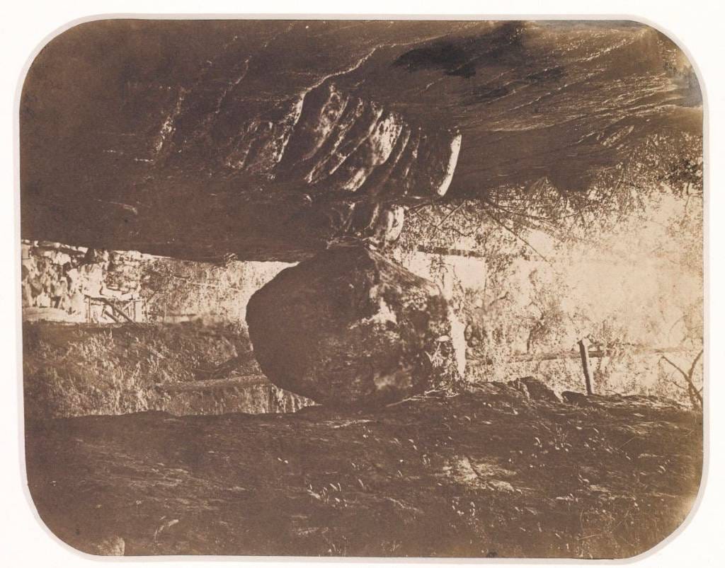 Sepia tinted photograph of boulder wedged between floor and roof of a cave