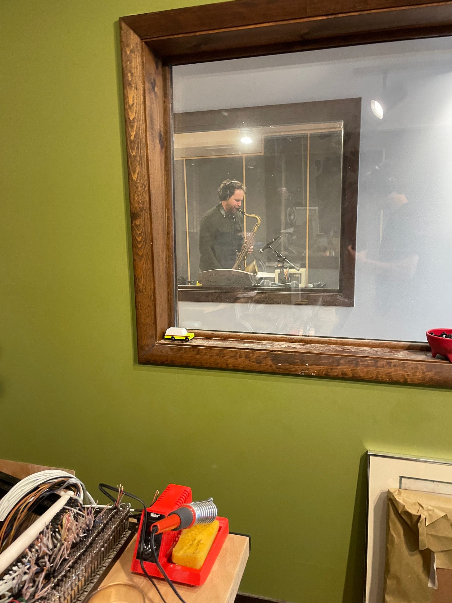 Hunter Diamond performing saxophone, seen through two layers of studio glass windows.
