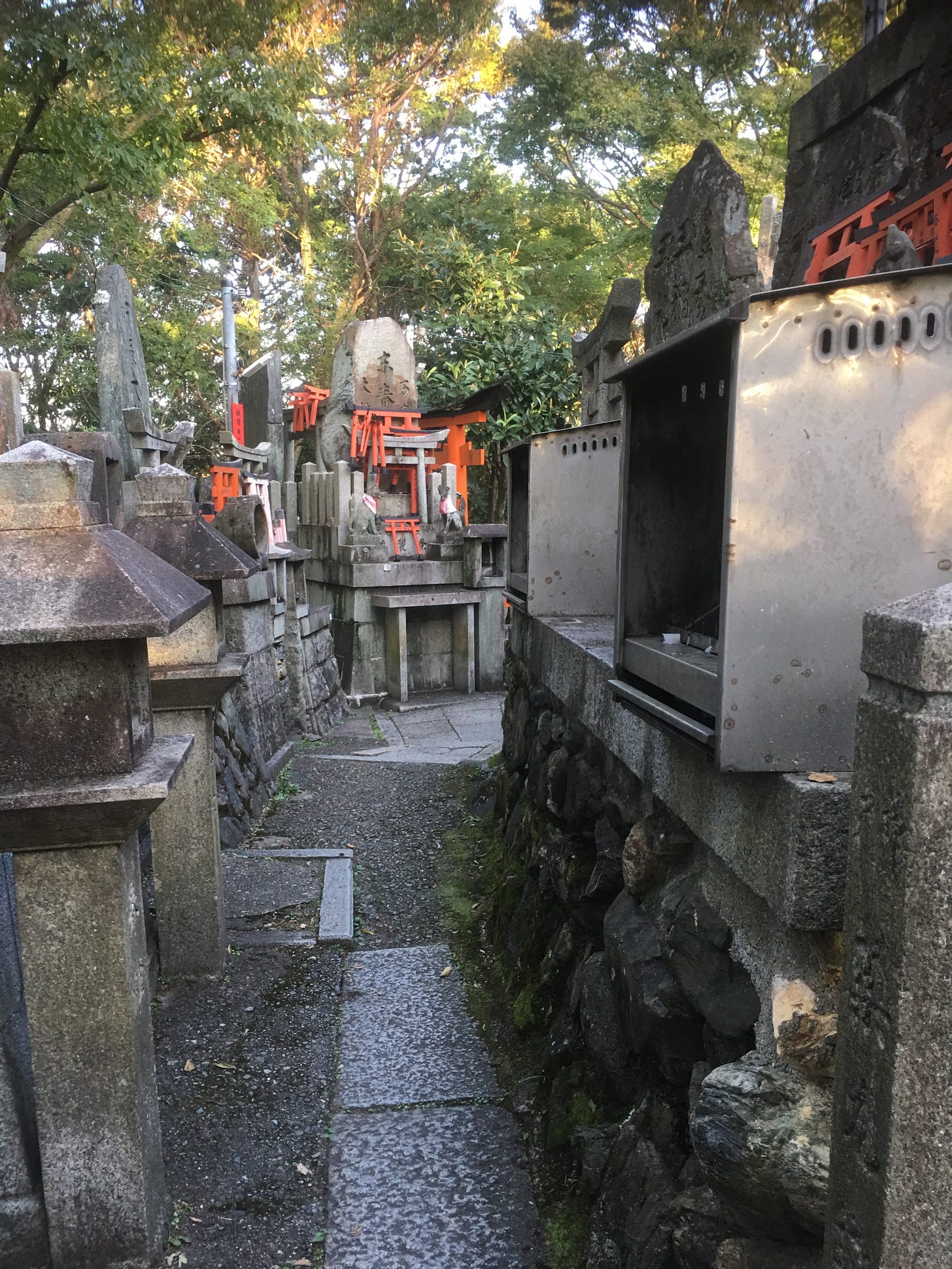 A narrow corridor with multiple shrines, including metal boxes for burning incense.