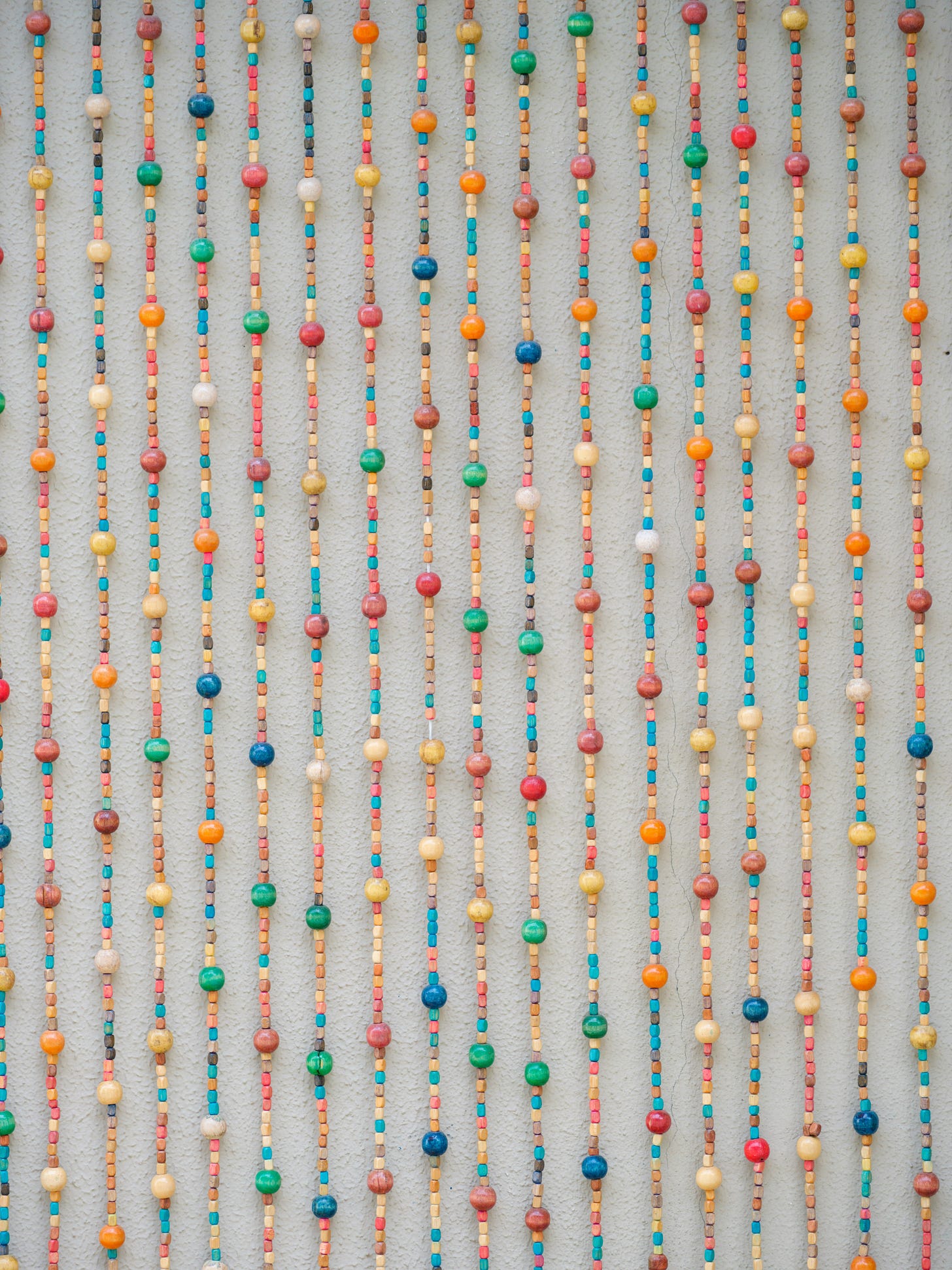 Vertical strands of colorful wooden beads on gray fabric, each strand representing accumulated daily marks over time through varied bead patterns.