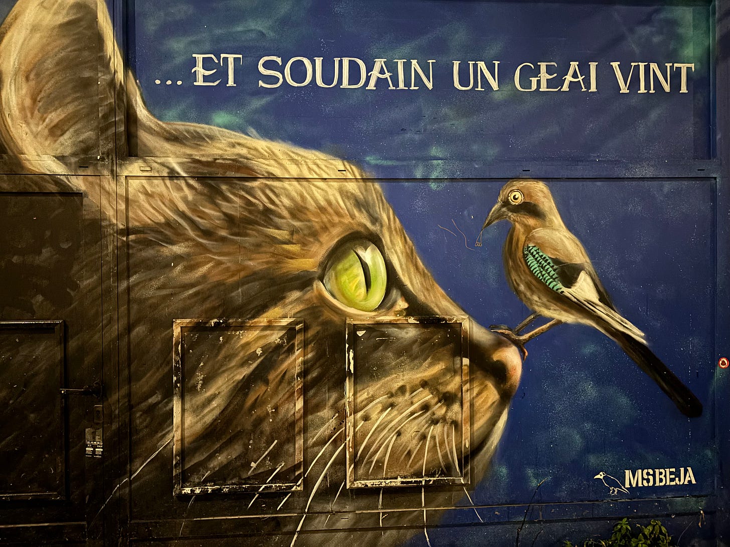 Mural featuring a tabby cat's head in profile, with a small jay perched on her nose. In cream capitals over a blue background, the text reads "... Et soudain un geai vint" (English Translation: "... And suddenly a jay came"