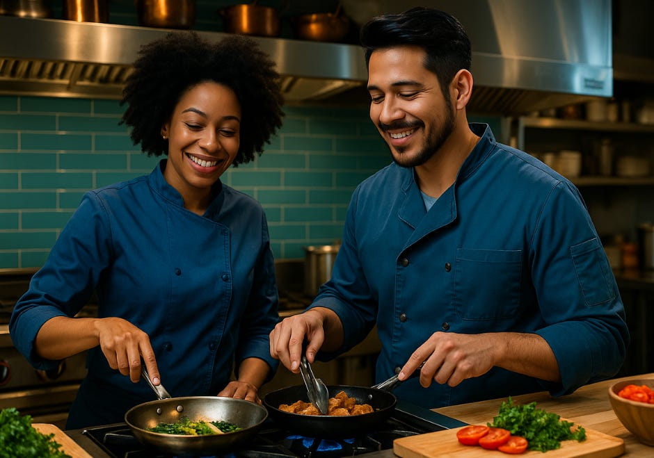Milo and Kate wearing chef coats, smiling behind the counter of a professional restaurant kitchen.