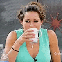 a woman is drinking a cup of coffee while wearing a blue tank top . a woman is drinking a cup of coffee while wearing a blue tank top .