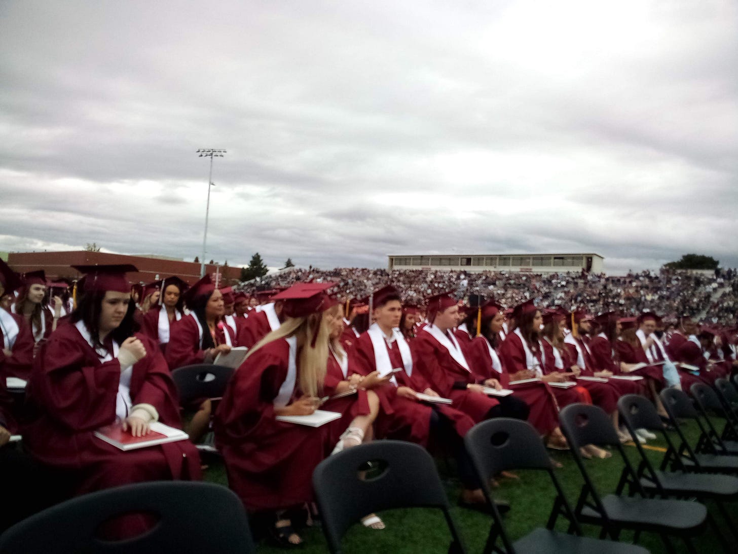 Graduates in caps and gowns seated on football field