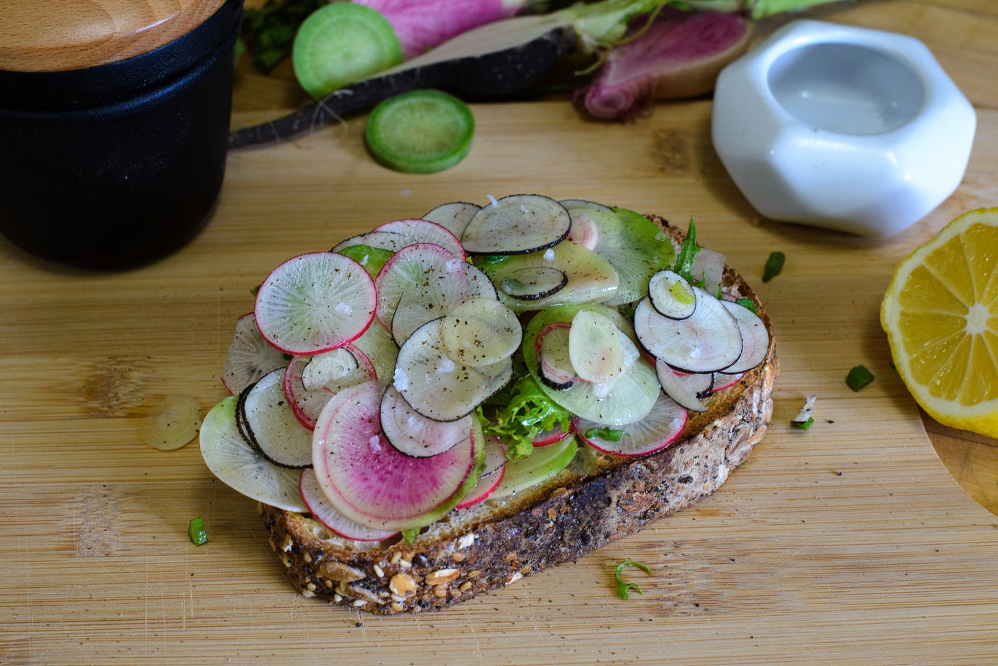 Radish salad toast on a cutting board with lemon, radishes, and salt.