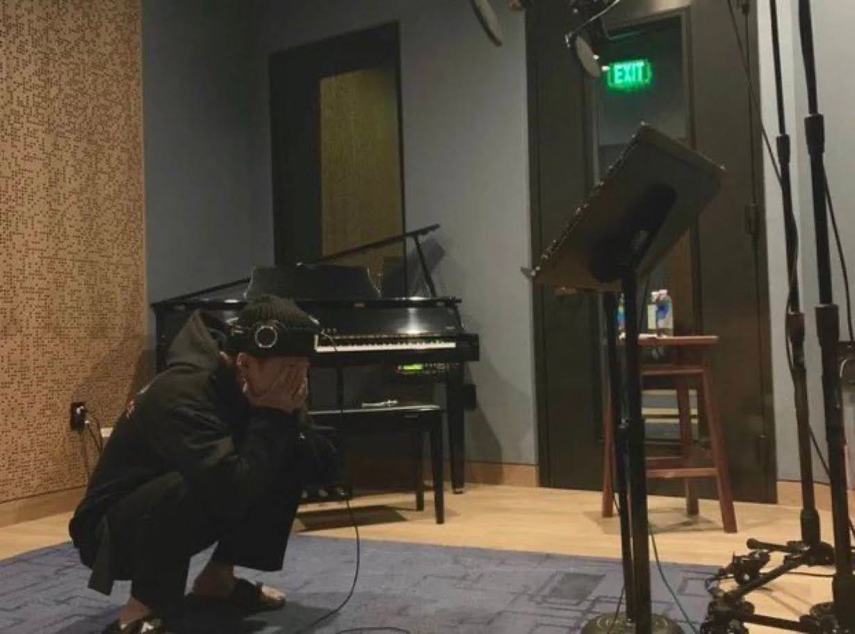 Min Yoongi of BTS deep squatting on the floor of a recording studio with his face in his hands