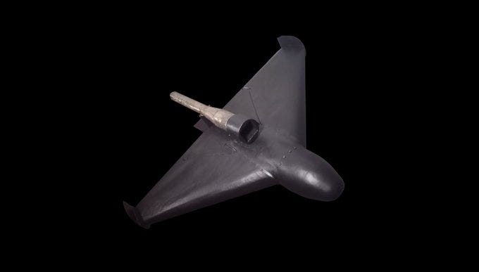 A sleek, dark-colored KROOK-1 drone with triangular wings and a cylindrical pulsejet engine mounted on top. The drone has a smooth, aerodynamic design. A sleek, dark-colored KROOK-1 drone with triangular wings and a cylindrical pulsejet engine mounted on top. The drone has a smooth, aerodynamic design.