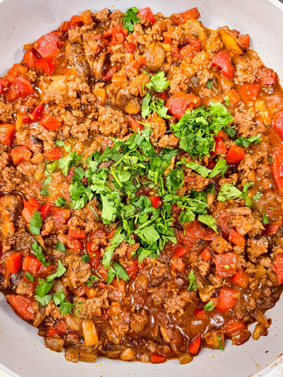 A skillet filled with cooked ground meat, diced red peppers, tomatoes, and onions, topped with fresh chopped cilantro.