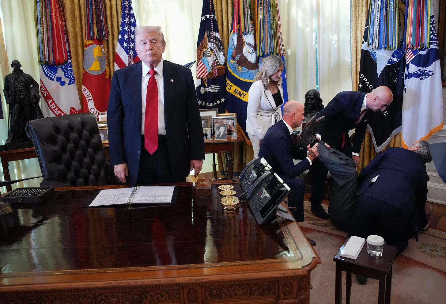 President Donald Trump stands by as attendees help an executive after he collapsed during an event on lowering drug prices in the Oval Office Thursday