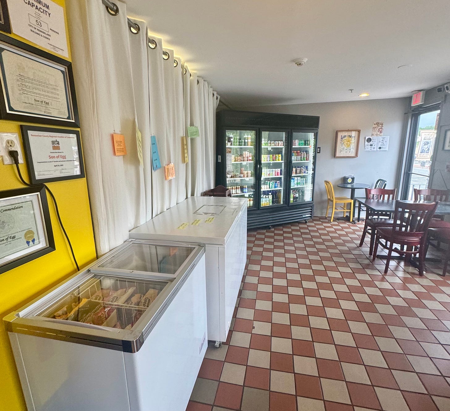 a tiled cafe space with refridgerators stocked with drinks and large freezers selling ice cream and frozen beef