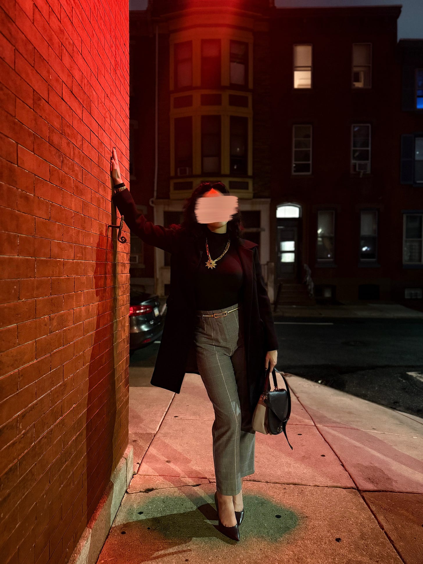 Once again, Elena is looking extra special in red light. It’s evening and she is paused on a city sidewalk, one hand against the brick building to her left, leaning slightly. The other hand is by her side, holding her bag. She’s looking right at the camera, head on, with a very sweet (read: tipsy) look that has been blurred because privacy. Her dark hair is down, wavy, and extra thick because the humidity was really doing the most. She’s wearing a black turtleneck, gray plaid high waisted pants, black pointy heels, and a black pea coat. Gold vintage jewelry and belt complete the look. Props to my photographer/date for catching such a nice shot, he was rewarded accordingly. 👏