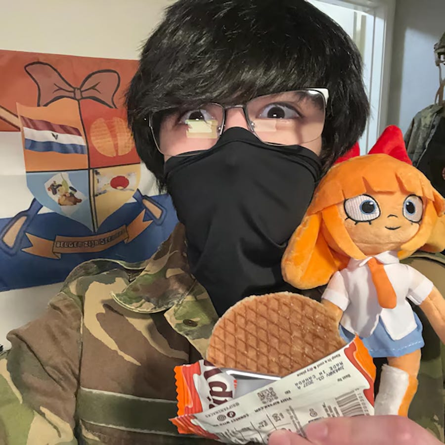 A man with his face covered in a camo outfit with a Mymy doll. 