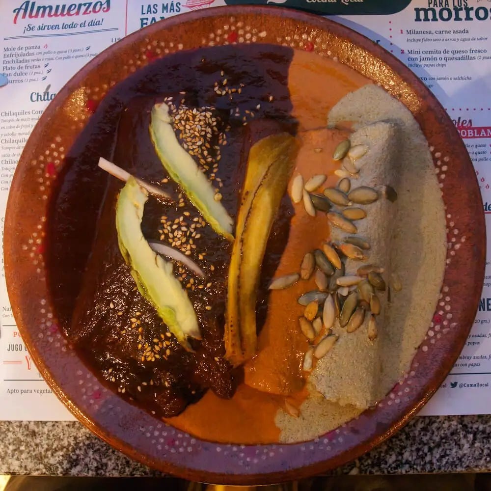 A plate of enchiladas smothered in three separate mole sauces - chocolate, red and beige